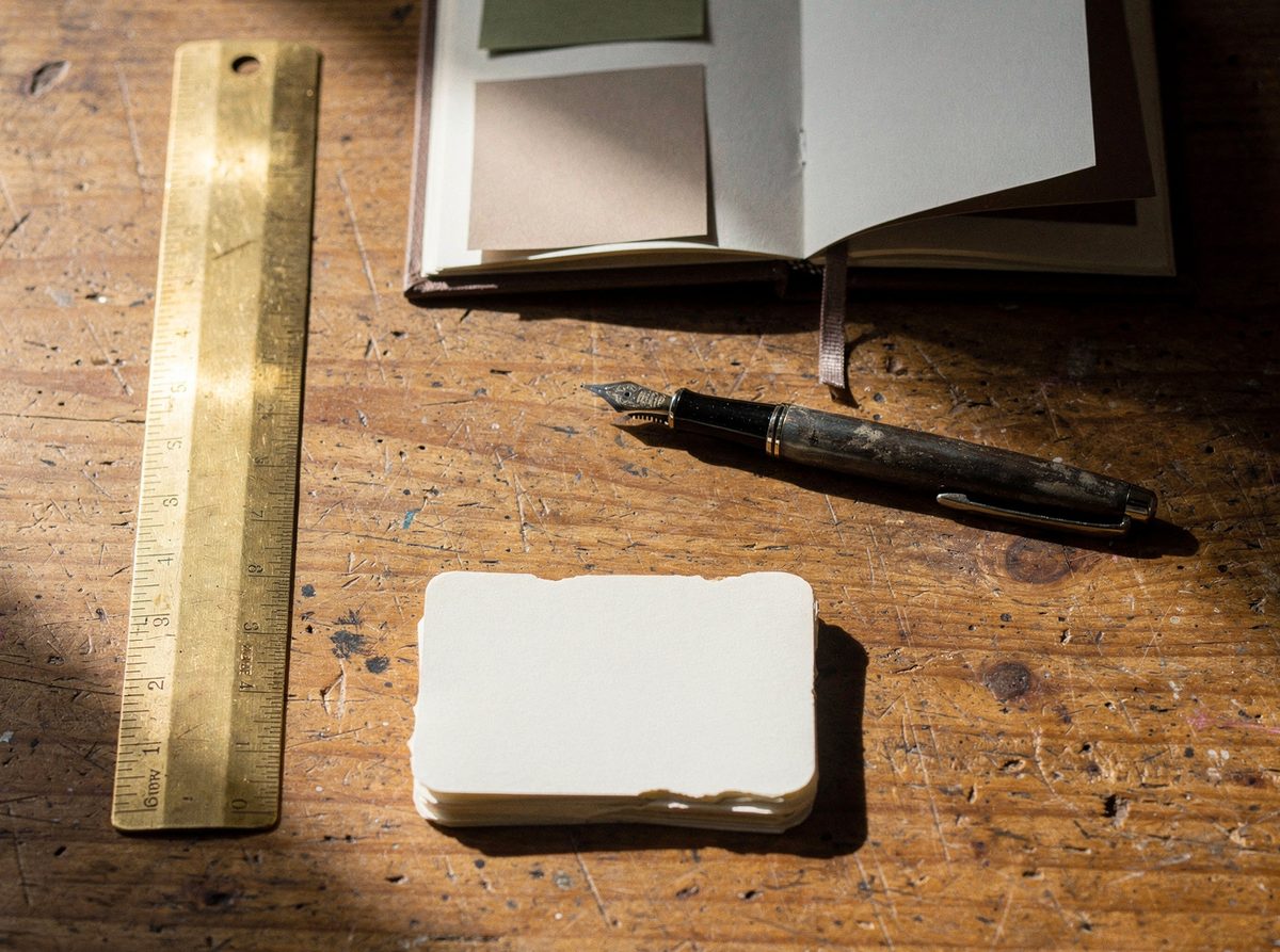 A consultant's desk holding a fountain pen, a brass ruler and an open swatch book.