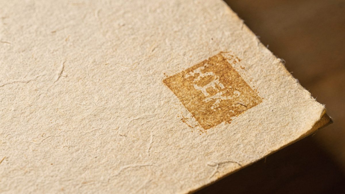 A close texture of aged paper grain with a faded ochre ink stamp mark.